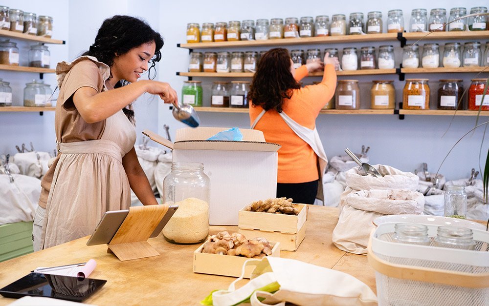 Imagem de duas mulheres organizando sua loja de produtos naturais com os produtos de boa procedência.